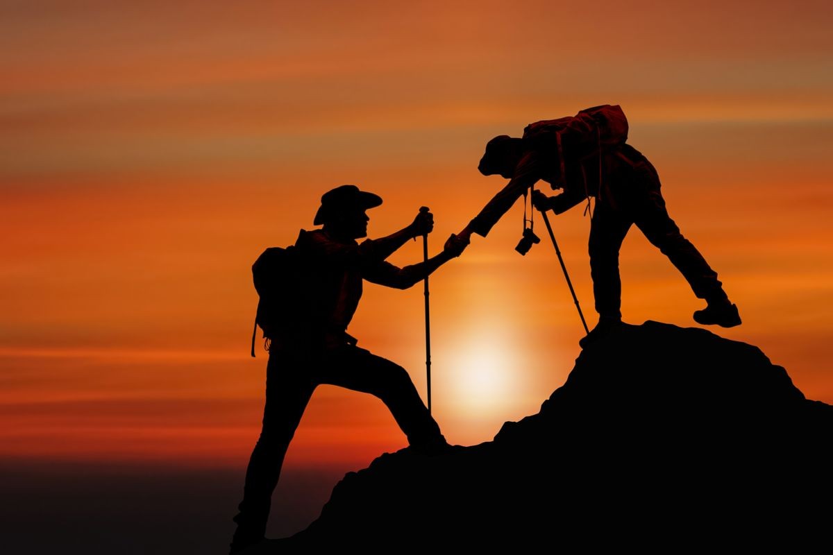 Two hikers successfully reaching the summit at sunset, illustrating teamwork and partnership in achieving investment goals with Luxe Living Homes' preferred equity and fund investments.