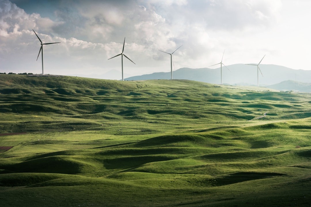Rolling green hills with eco-friendly wind turbines generating renewable energy, symbolizing Luxe Living Homes' commitment to impact investments in sustainable development.